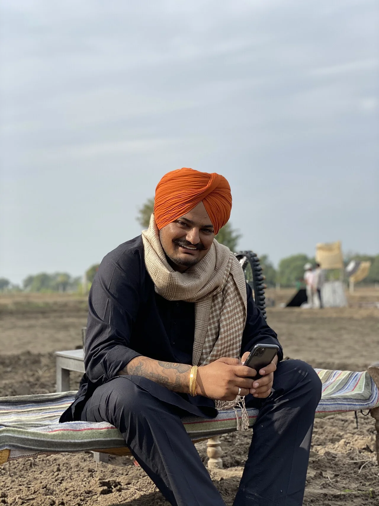 Sidhu Moose Wala seated on a charpai in a field during the shoot of his film Moosa Jatt