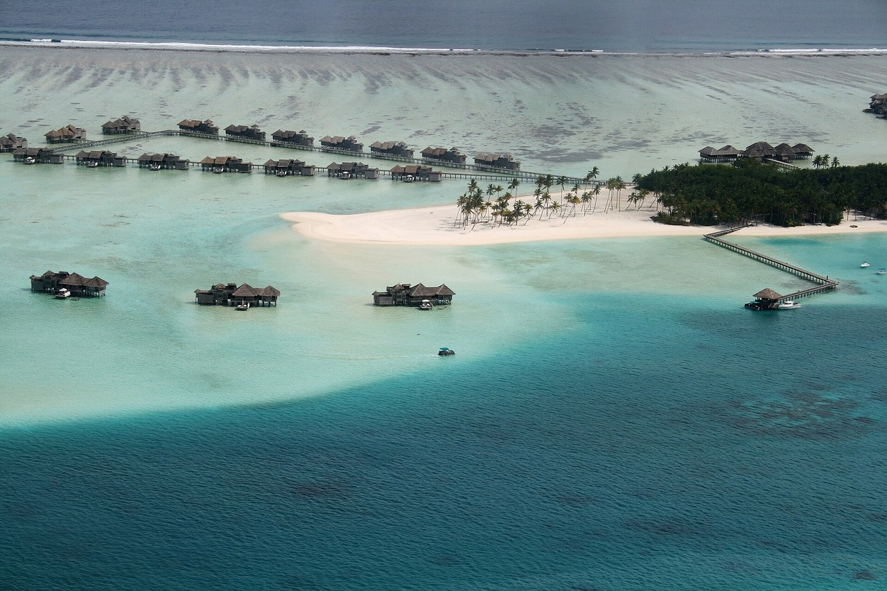 Aerial view of a Maldives resort island with overwater villas in a turquoise lagoon